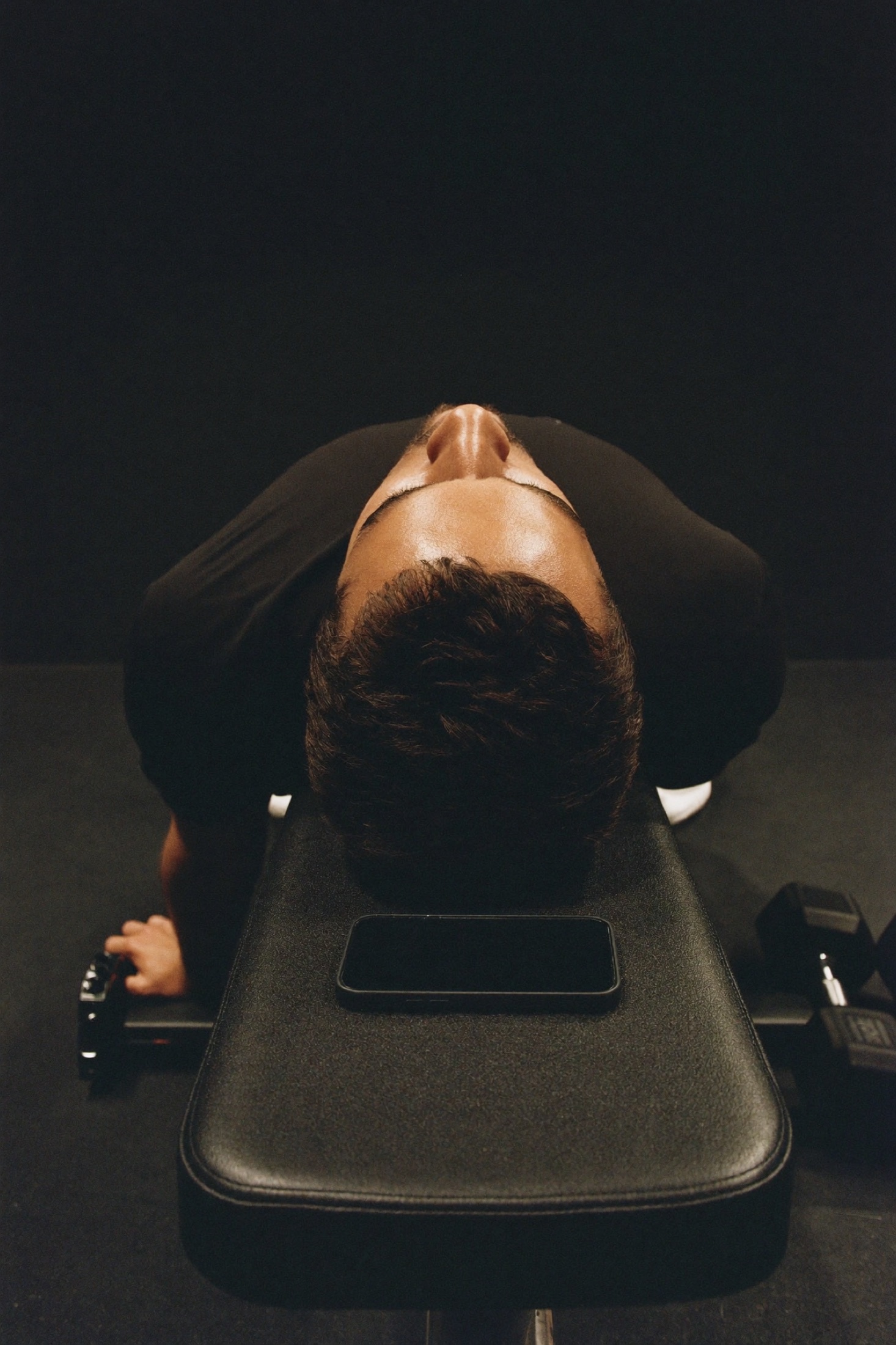 A lifter resting on a bench with a phone beside him